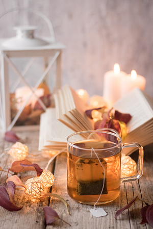 A mug of herbal tea with a book and two candles in the background